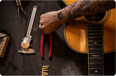 A luthier carefully adjusting the neck of an acoustic guitar in a well-lit workshop filled with tools and guitar parts.